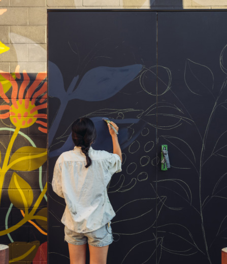 A woman painting a plant on the wall at Artbeatz art class